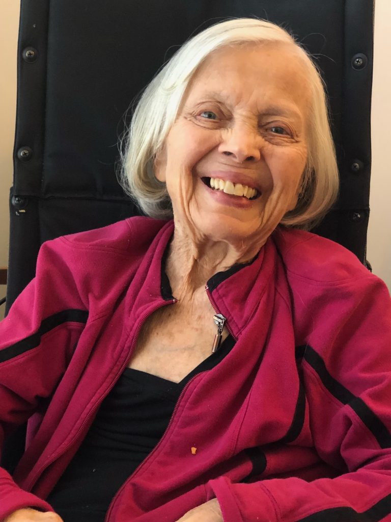 image: elderly woman with silver bobbed haircut, with a big smile, wearing a dark red jacket